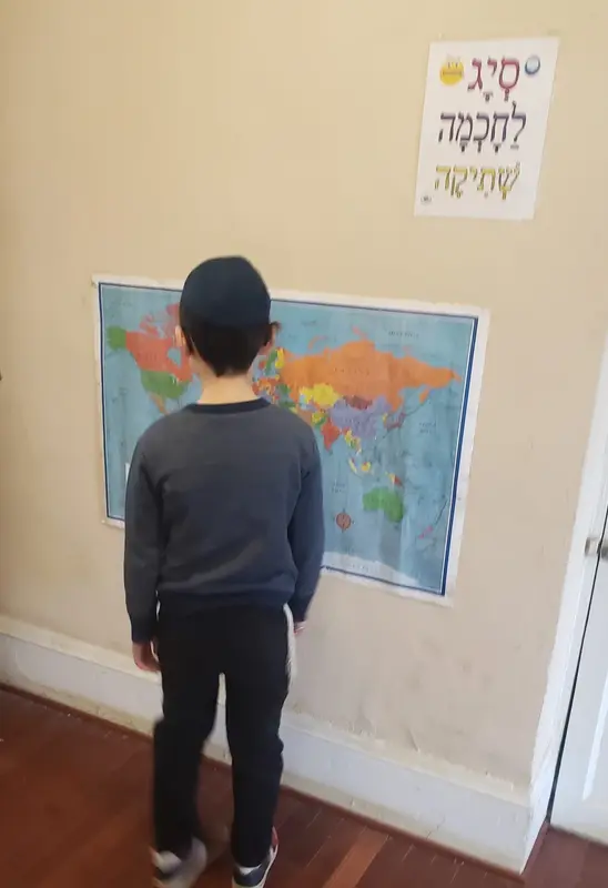 A young boy studying a world map on the classroom wall