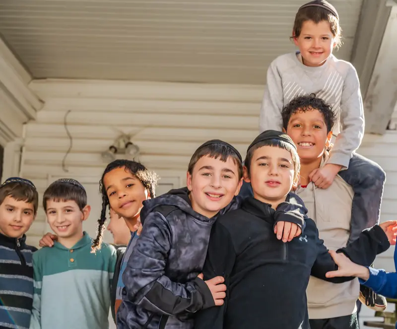 A group of smiling boys crowded together on a porch, one riding on another's shoulders