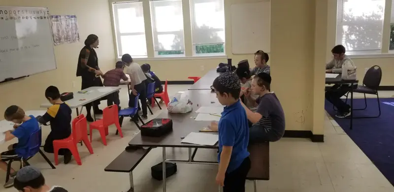 Children seated at tables while a teacher works at the whiteboard