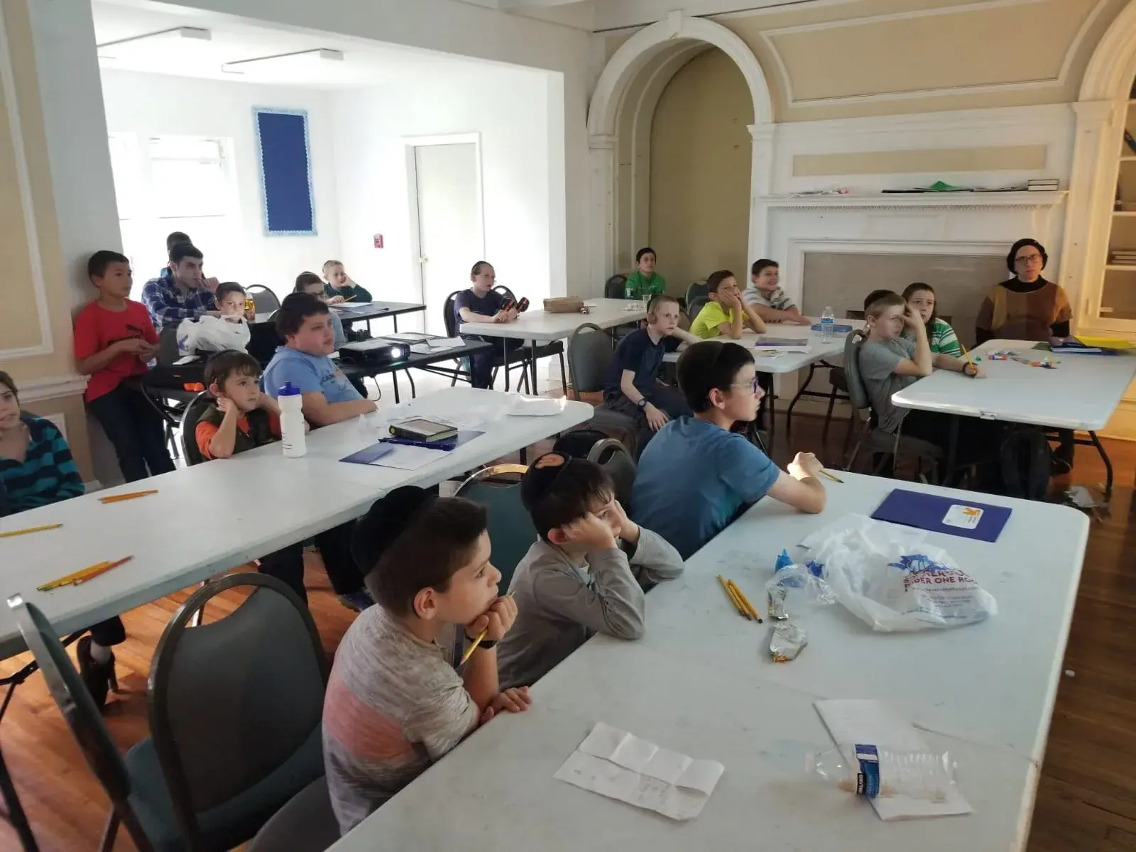 A class of boys at tables listening to their teacher at the front of the room