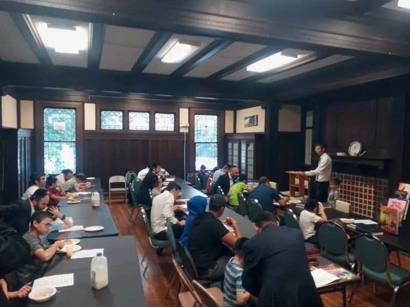 Men and boys at a meal in the wood-panelled hall while a speaker addresses the room