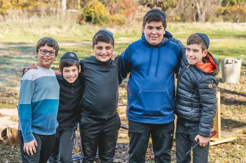 Five smiling boys in kippot standing together outdoors