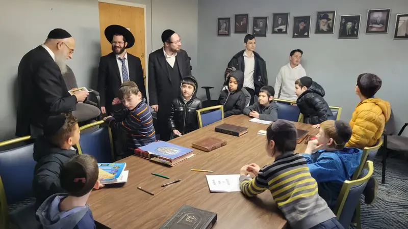 A teacher and boys learning together around a table of open seforim
