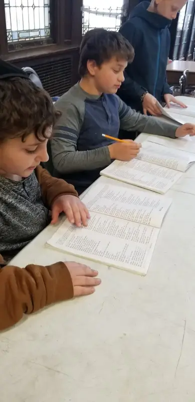 Boys reading from open texts at a long table