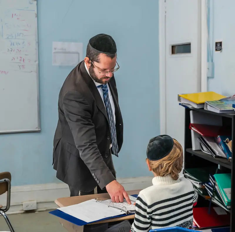 A teacher pointing out something on a worksheet at a student's desk