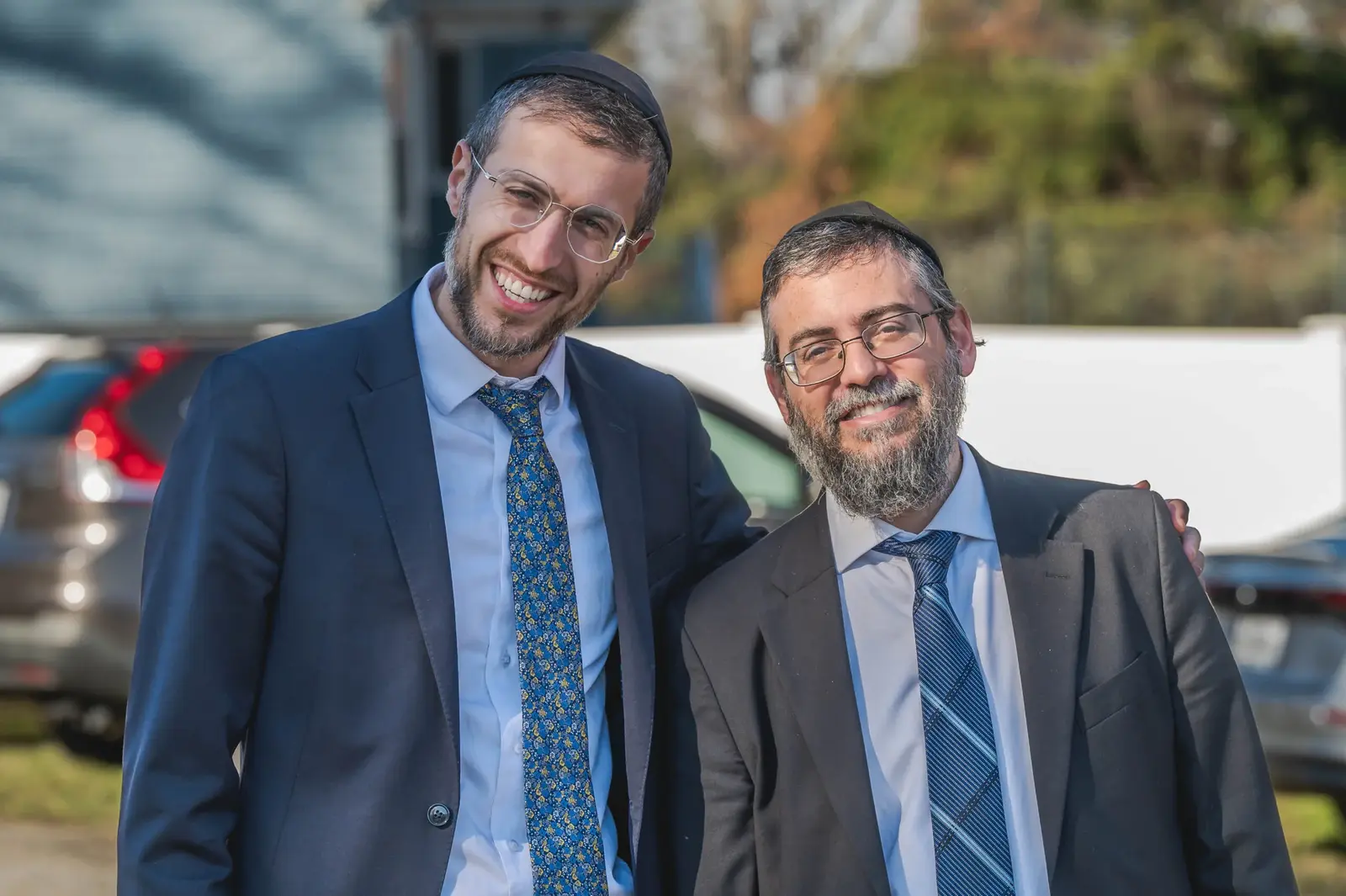 Two smiling men in suits standing outside the school on a sunny day