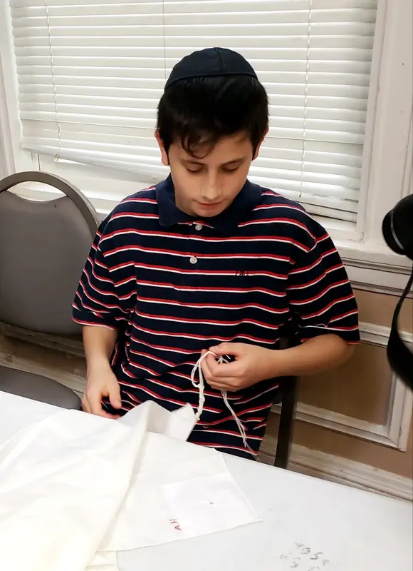 A student tying tzitzis strings at a table